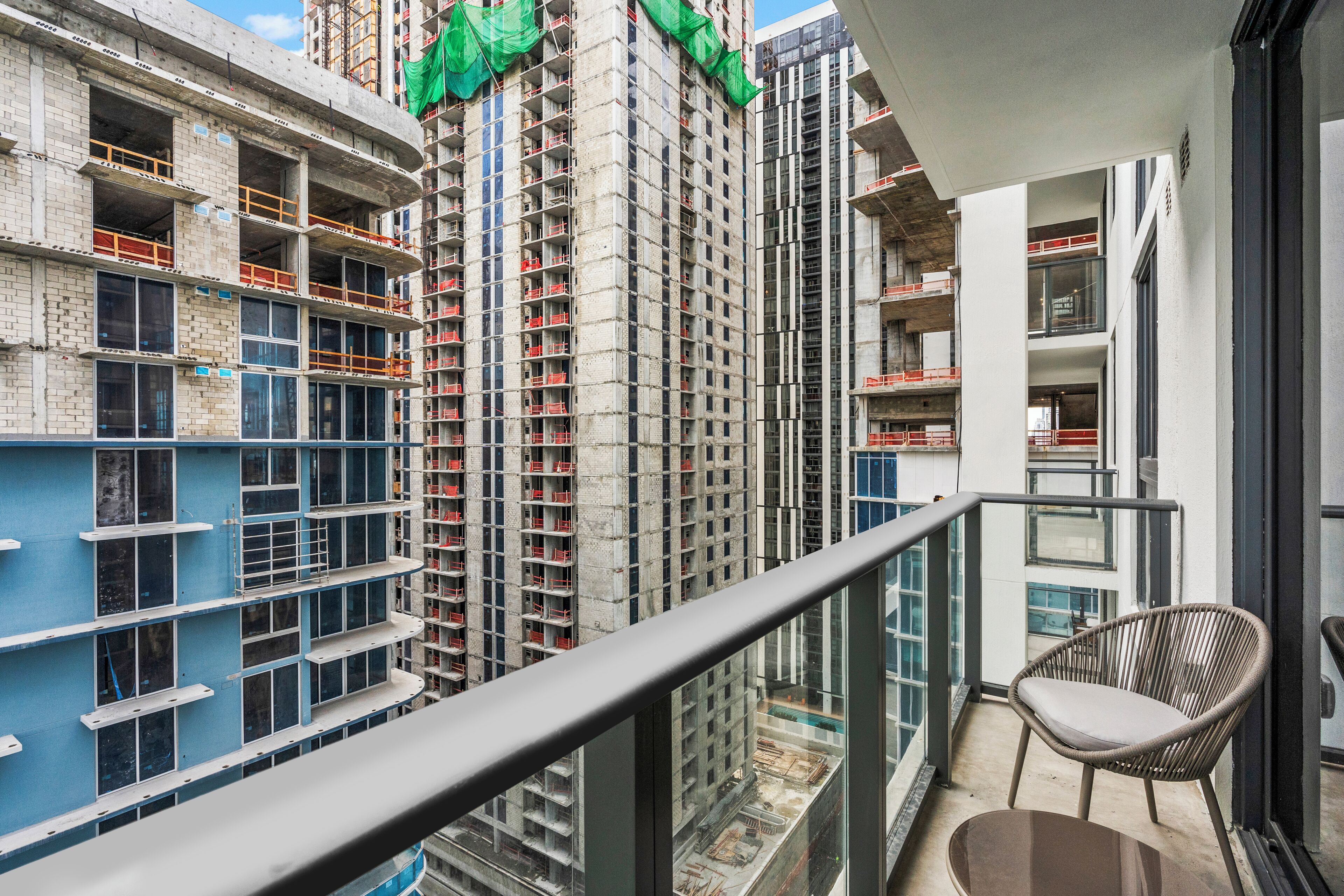 A balcony with a chair, overlooking a construction site with multiple high-rise buildings.