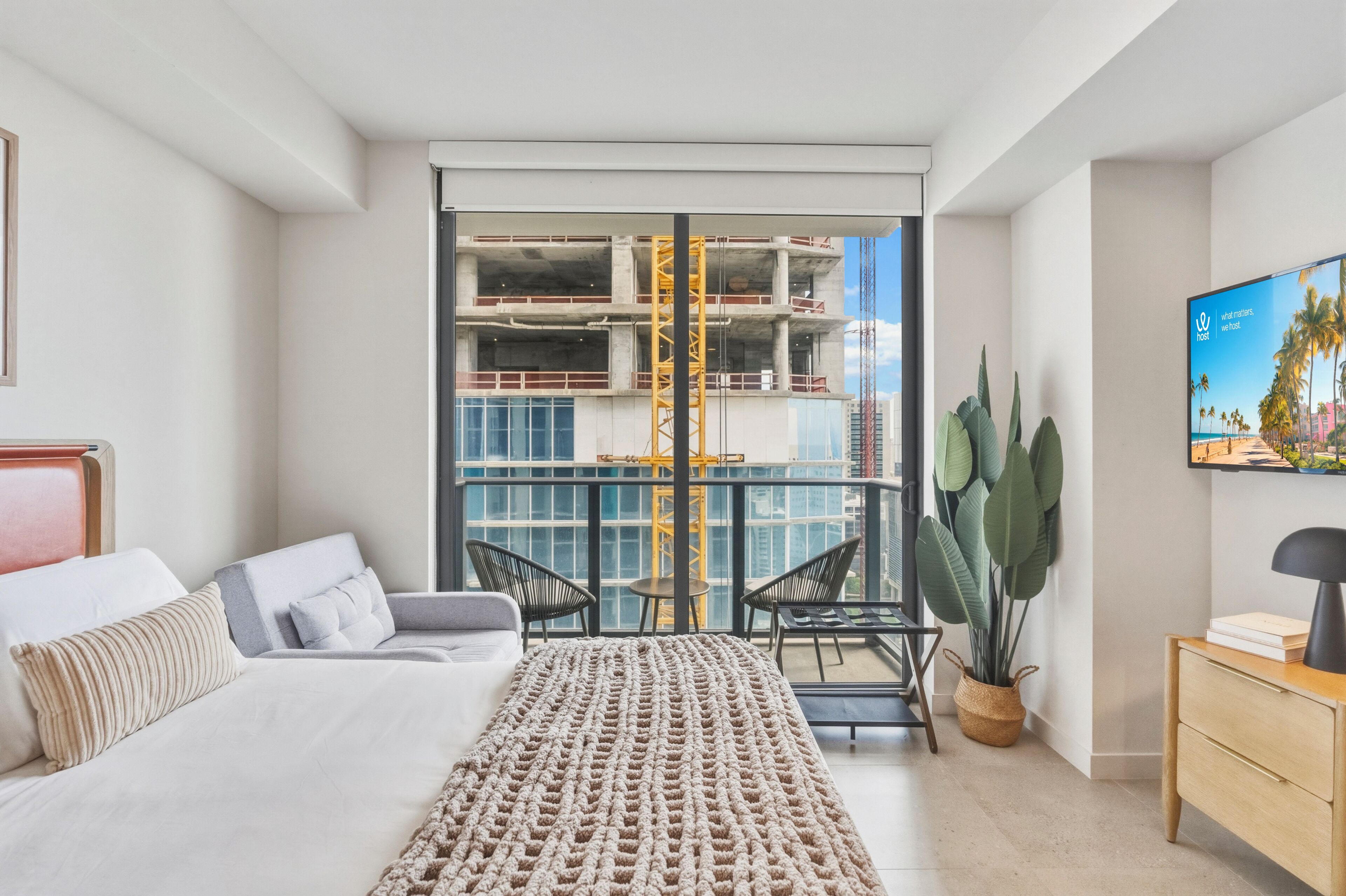 Een moderne hotelkamer met balkon, een bed, bureau en een groot raam met uitzicht op een bouwplaats.