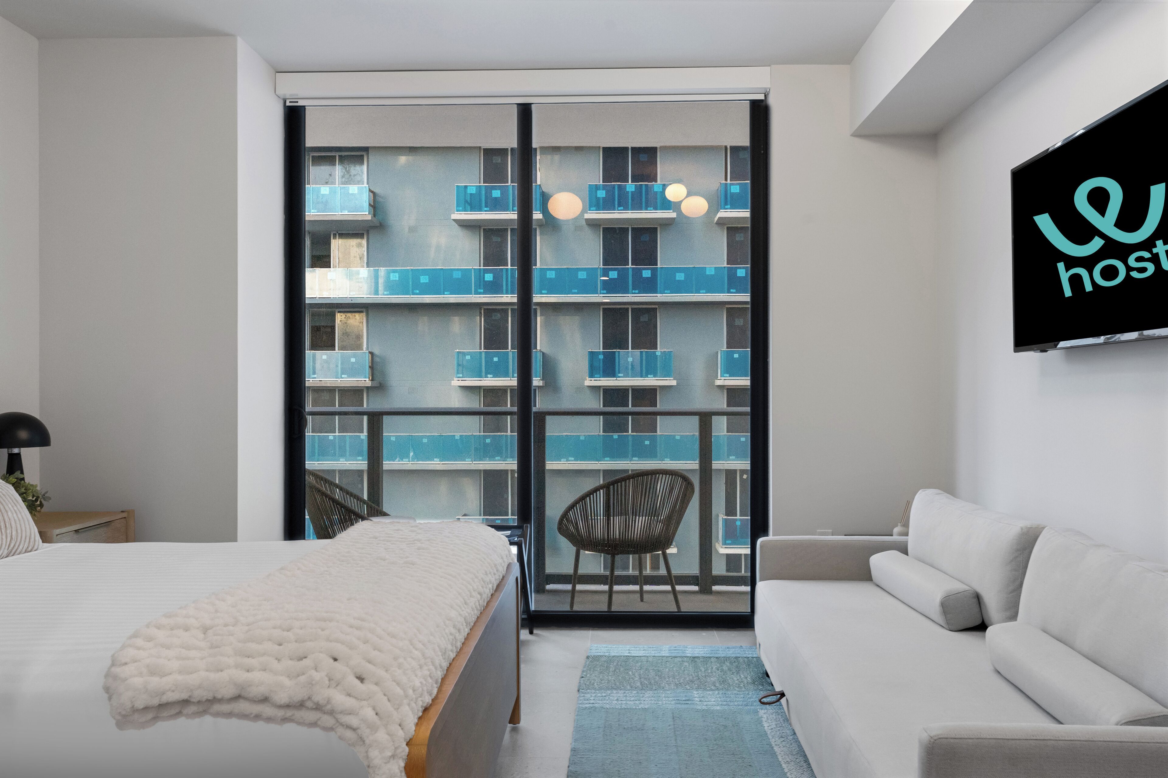 Une chambre d’hôtel moderne avec un grand lit, un canapé, un fauteuil et un balcon doté de balustrades bleues.