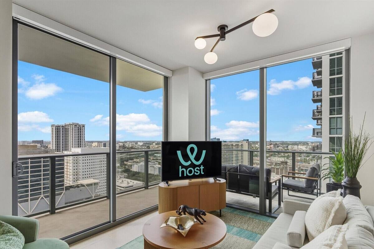 Un salon moderne doté d’un grand téléviseur, d’un canapé, d’une table basse et d’un balcon offrant une vue sur la ville.