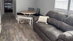 A compact living space with a grey leather sofa, a small round table, and a bench. A bunk bed is visible in the background. - 3 blocks from boat dock see the festivals and bands from back porc (Homosassa)