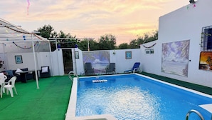 A swimming pool with a green artificial turf area, lounge chairs, and a white building with murals. - The House of Flamenco (Cañada del Rabadán)