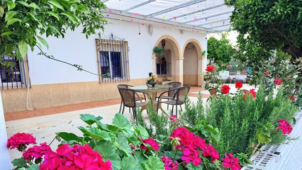 A patio with a table and chairs, surrounded by vibrant flowers and greenery. - The House of Flamenco (Cañada del Rabadán)