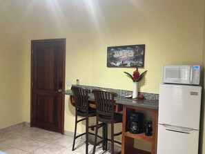 A small kitchen with a refrigerator, microwave, and a coffee maker on the counter. There is a door on the left and a painting on the wall. - Come hang out on the dock and watch dolphins (Sandy Bay)