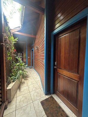 Un couloir avec une porte en bois et des moulures bleues, un sol carrelé et un bac à fleurs contenant des plantes vertes.