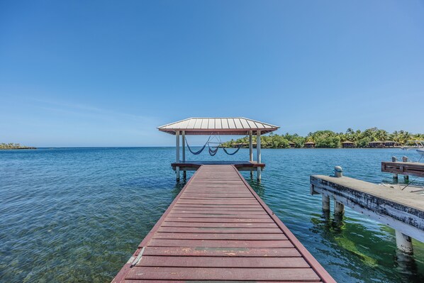 A wooden pier leading to a gazebo over water with clear skies. - Come hang out on the dock and watch dolphins (Sandy Bay)