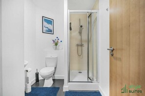 Een badkamer met een glazen douchecabine, toilet, wastafel en een lijst met een foto aan de muur.