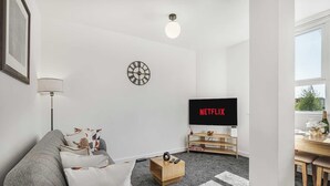 Ein modernes Wohnzimmer mit grauem Sofa, einem Couchtisch, einem Fernseher und einer Uhr an der Wand.
