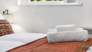 Ein ordentlich bezogenes Bett mit weißen Leinentüchern und einer braunen Tagesdecke.