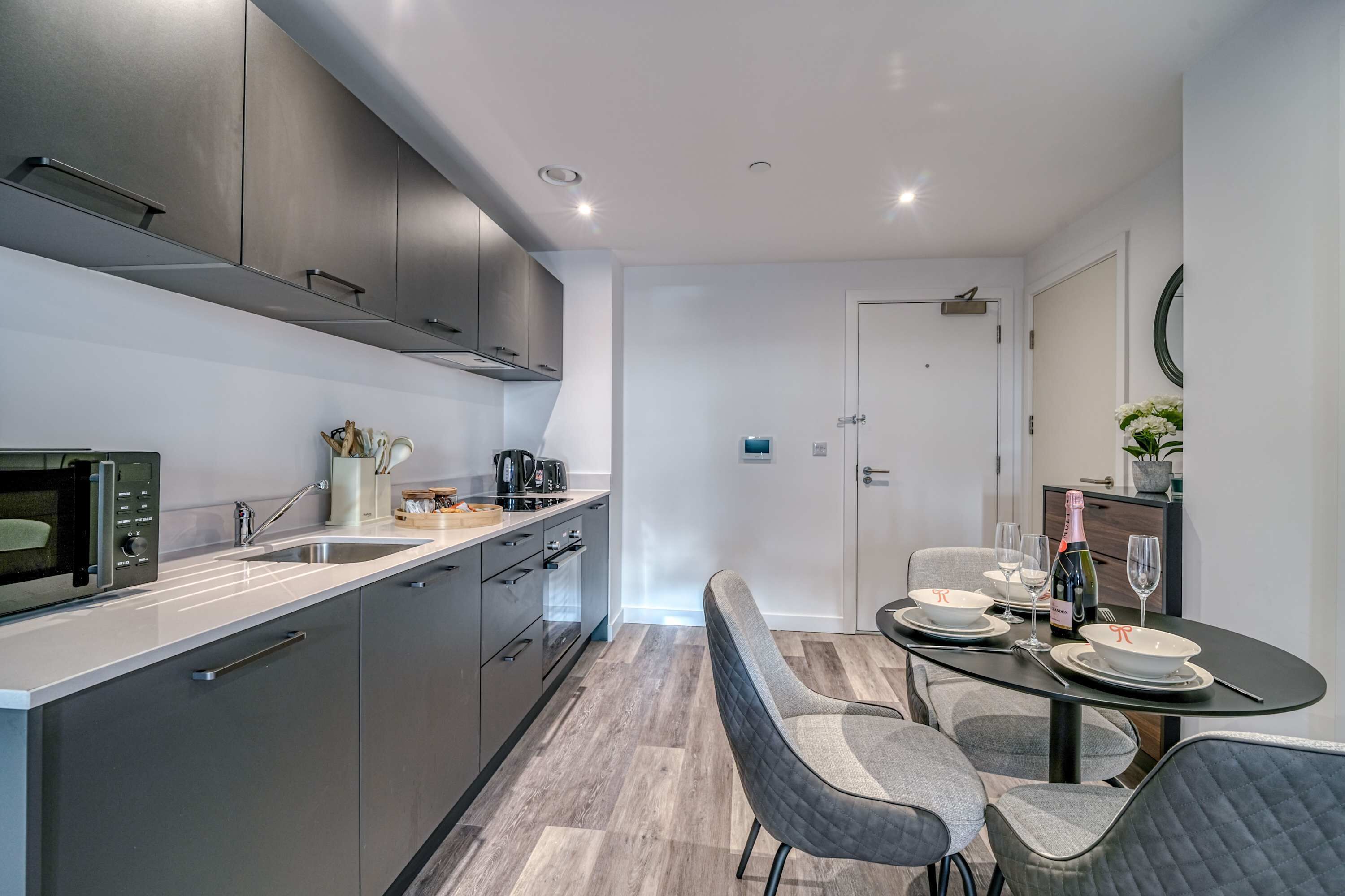 A modern kitchen with grey cabinets, a microwave, and a dining area with a table set for two.