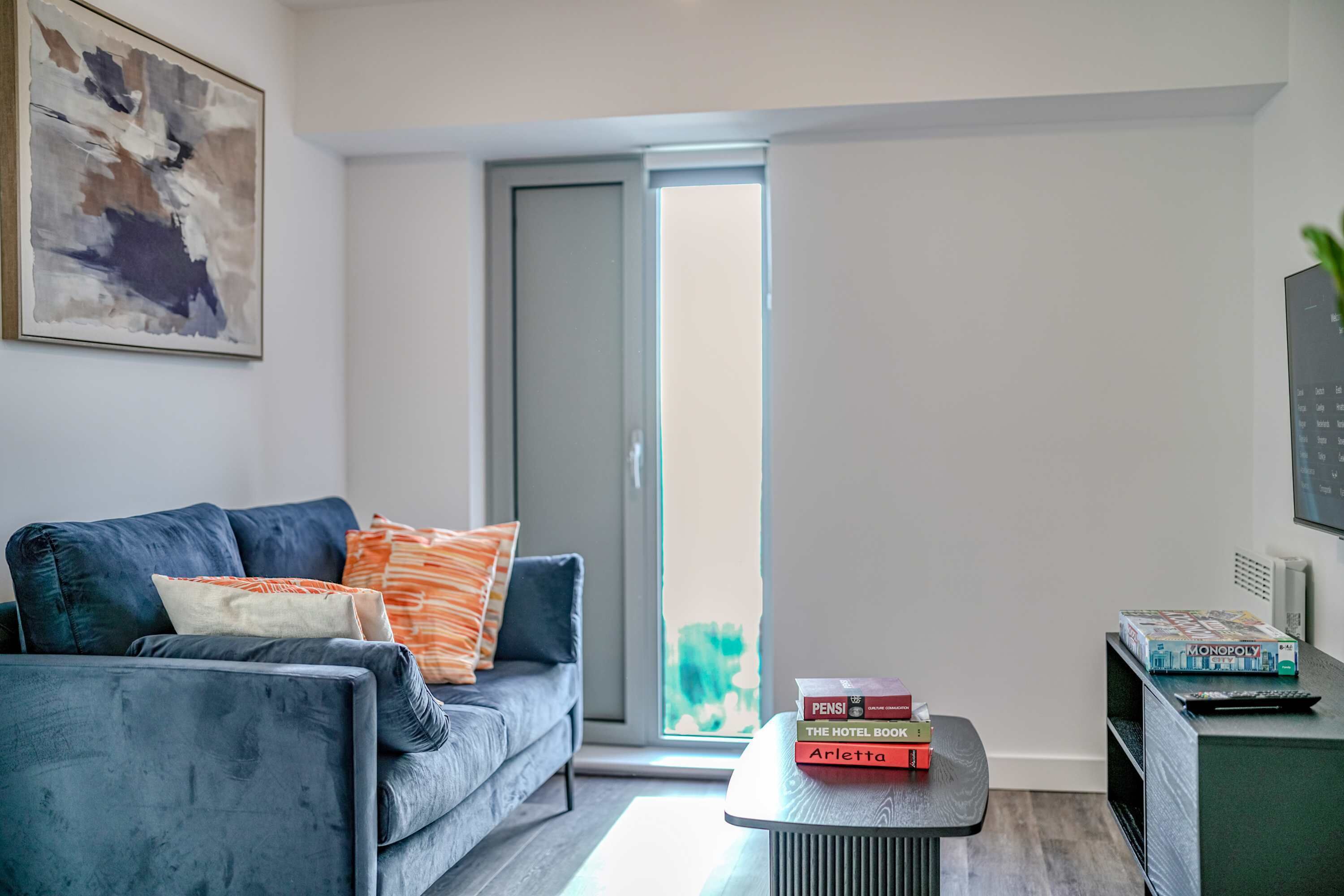 A modern living room with a grey sofa, a coffee table, and a bookshelf with books and a Monopoly game.