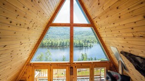 A triangular wooden cabin with a large window offering a view of a lake and forest.