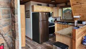 A modern kitchen with wooden cabinets, a stainless steel refrigerator, and a stone wall.
