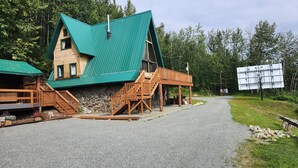 A chalet-style building with a steep green roof, wooden deck, and a stone foundation.