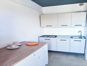 Una cocina con armarios blancos, encimera de madera, cocina a gas y un lavabo.