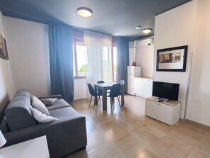 Una sala moderna con sofá, mesa de comedor, sillas, kitchenette y televisor.