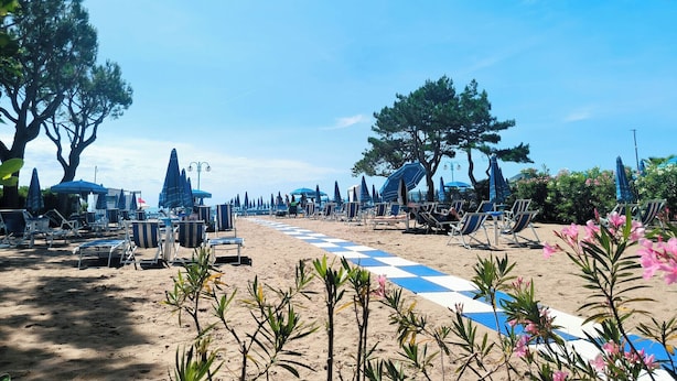 A beach with lounge chairs and umbrellas, a checkered path, and trees. - Cozy Studio Near the Beach (Jesolo)