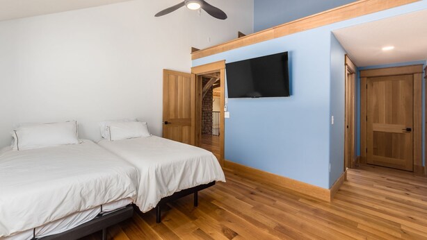 Ein Schlafzimmer mit einem Bett, einem Deckenventilator, einem an der Wand montierten Fernseher und Holztüren.