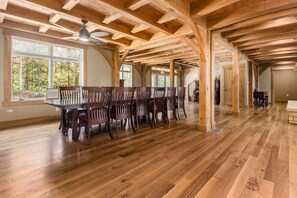 A spacious dining area with a long wooden table and chairs, large windows with a view of trees, and a high ceiling with exposed wooden beams. - Timberframe Lodge| Hocking Hills, Luxury, Pond (Rockbridge)