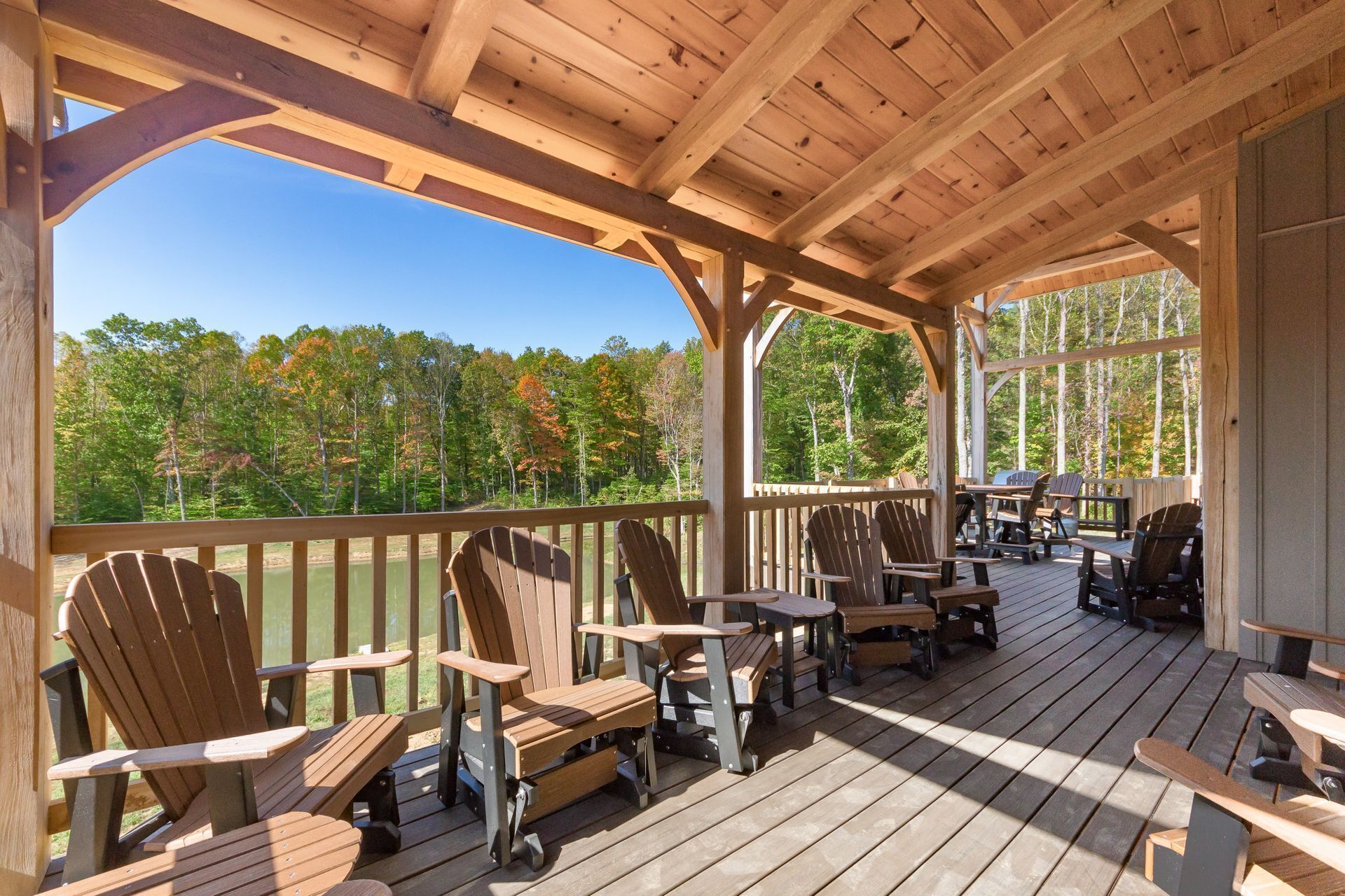 Een houten terras met Adirondack-stoelen en tafels, uitkijkend op een bebost gebied.