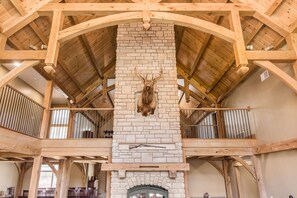 A rustic interior with a stone fireplace, wooden beams, and a deer head mounted on the wall. - Timberframe Lodge| Hocking Hills, Luxury, Pond (Rockbridge)