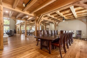 A spacious dining area with a long wooden table and chairs, high wooden ceilings, and a view of the kitchen in the background. - Timberframe Lodge| Hocking Hills, Luxury, Pond (Rockbridge)