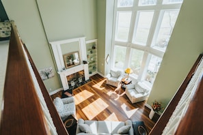 A spacious living room with a fireplace, wooden flooring, and large windows. - Hocking Manor | Hocking Hills, 8BR, Indoor Pool (Rockbridge)