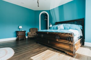 Une chambre à coucher avec un grand lit, une table de chevet, une chaise et un miroir décoratif.