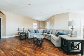Un salon spacieux avec un canapé d’angle, une table basse ronde et un plancher en bois.