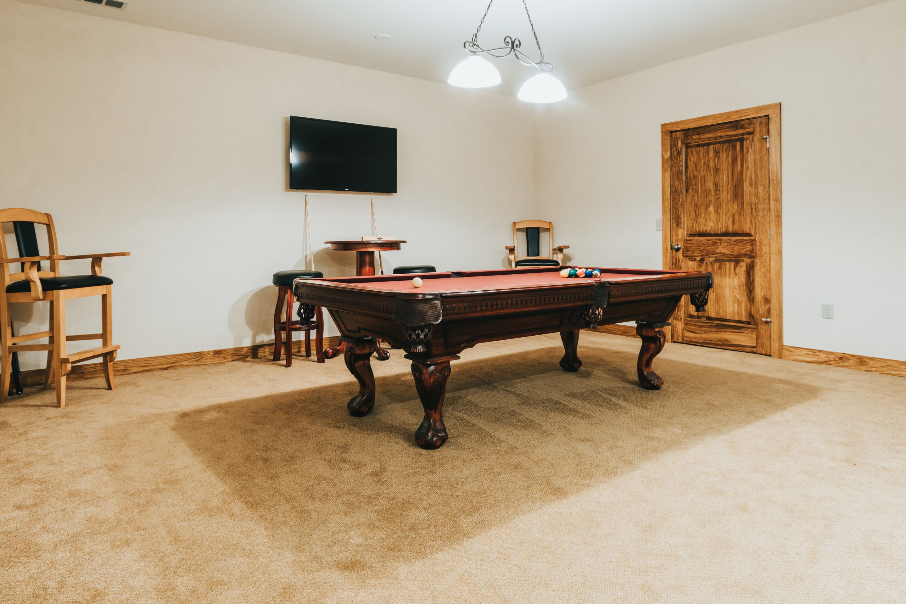 A room with a pool table, two chairs, a television mounted on the wall, and a wooden door.