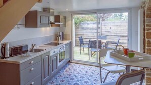 Et kompakt køkken med indbygget mikroovn, ovn og vask, et spiseområde med bord og stole, samt en skydedør af glas der fører ud til en terrasse med udendørs møbler.