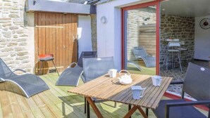En terrasse med et træbord og stole, en stenvæg og en trædør.