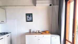 A compact kitchen with white cabinets, a small refrigerator, and a framed picture on the wall. - Cozy Studio With Balcony (Jesolo)