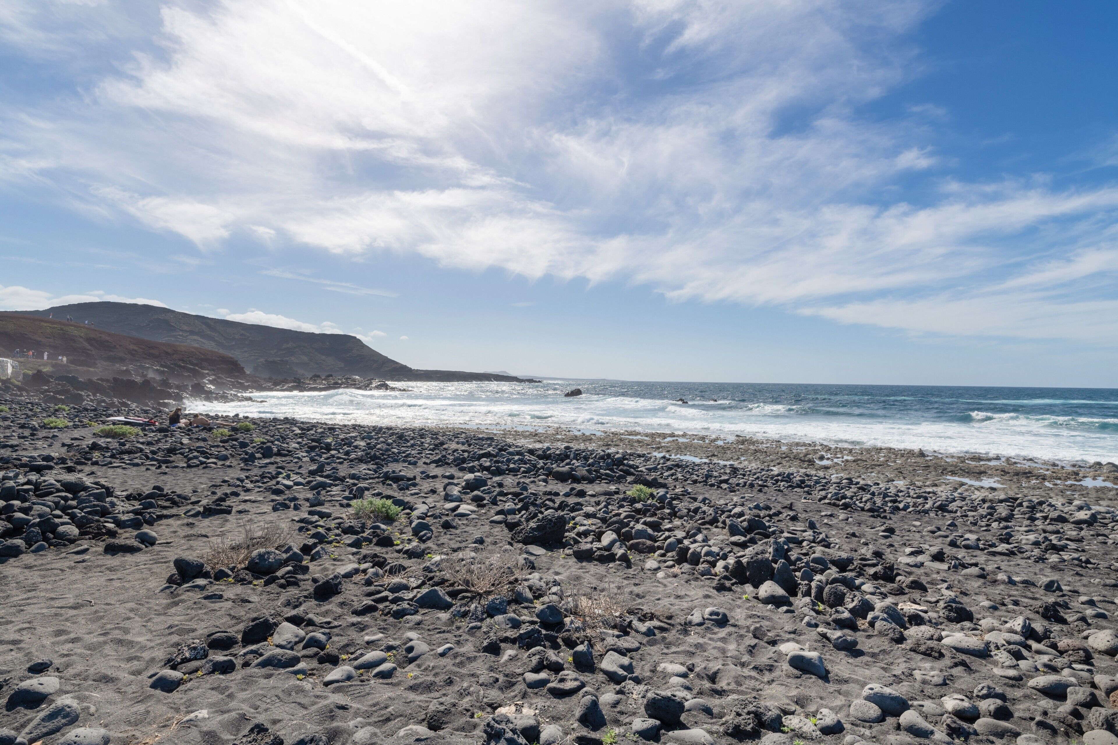 Una playa rocosa con olas, cielo despejado y montañas a lo lejos.