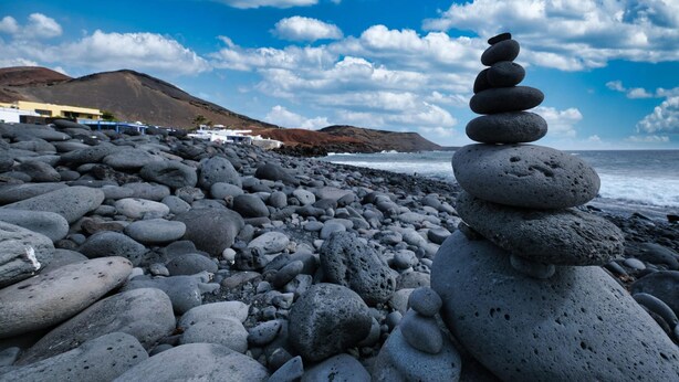 Una playa rocosa con un montículo de piedras en primer plano y un edificio al fondo.