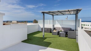 Una terraza en la azotea con pérgola, mobiliario exterior y vista al mar.