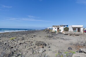 Een rotsachtig strand met gebouwen, waarvan sommige blauwe daken hebben, en de oceaan op de achtergrond.