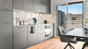 A modern kitchen with grey cabinets, a marble backsplash, and a dining area with a table and chairs. - Appartement B3 13 (Avenches)