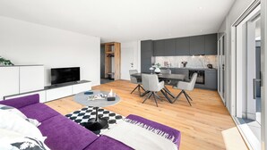 A modern living space with a sofa, dining table, and kitchen area. - Appartement B3 13 (Avenches)