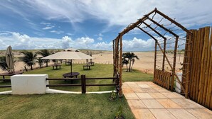 En terrasse ved stranden med borde, parasoller og en træport, der fører til stranden.