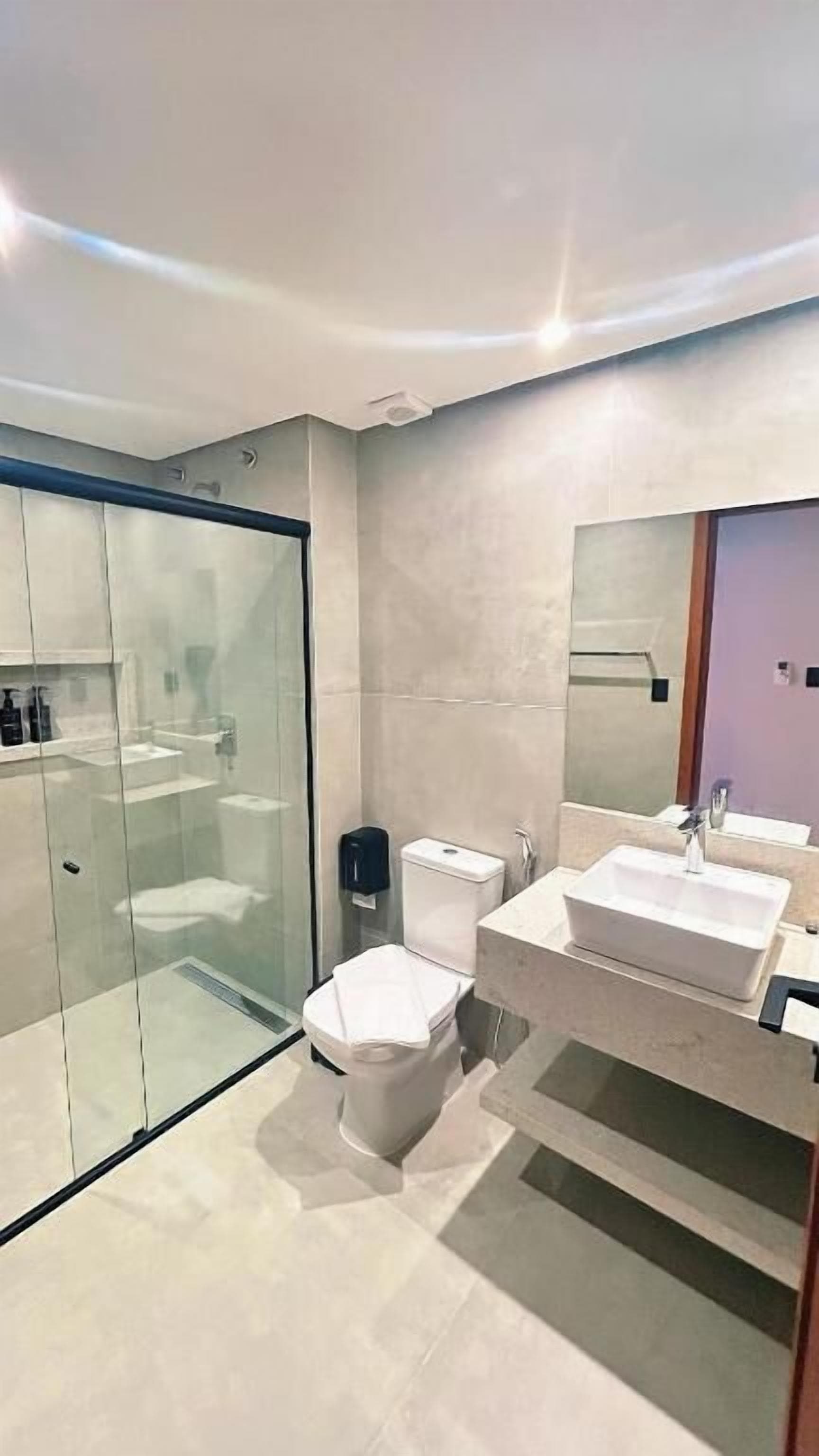 Casa de banho moderna com cabine de duche em vidro, sanita e lavatório com espelho.