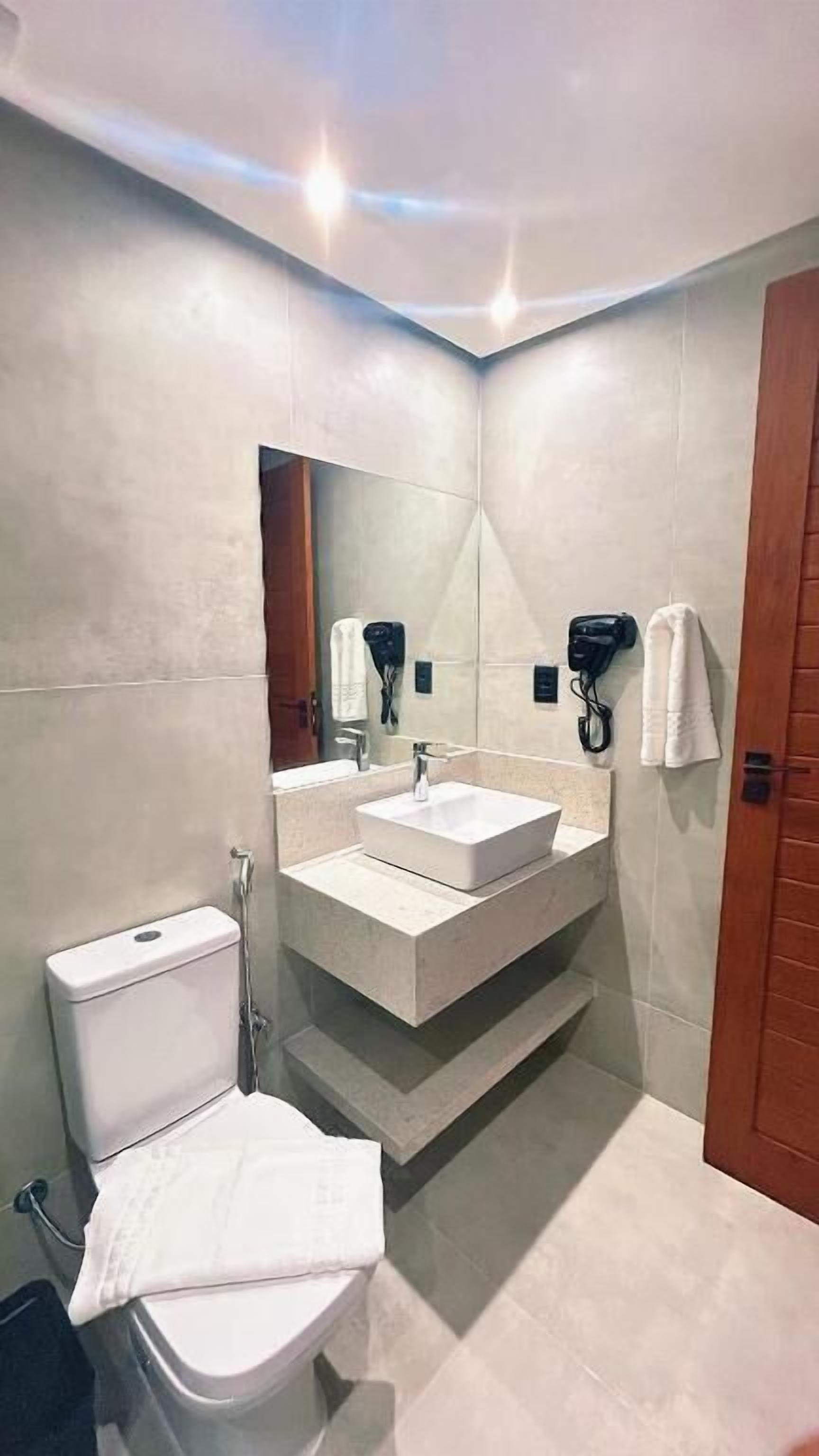 Un baño moderno con inodoro, lavamanos y espejo. Hay toallas colgadas en la pared y una zona de ducha.