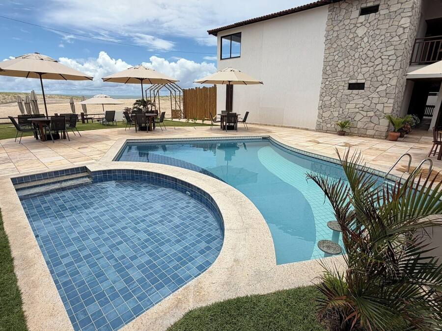 A swimming pool with a curved edge, surrounded by a patio area with outdoor furniture and umbrellas.