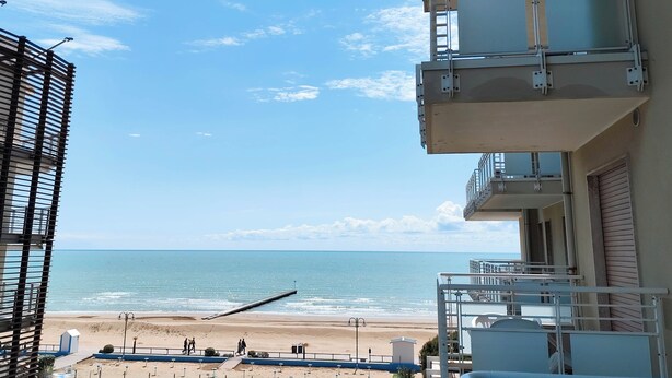 A beachfront hotel with balconies overlooking the sea, a pier, and a sandy beach. - Comfortable Studio by the sea (Jesolo)