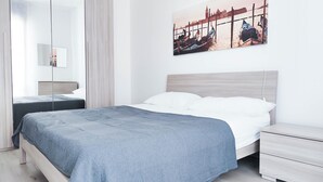 A modern bedroom with a large bed, a bedside table, a nightstand, and a wall-mounted TV. - Comfortable Studio by the sea (Jesolo)