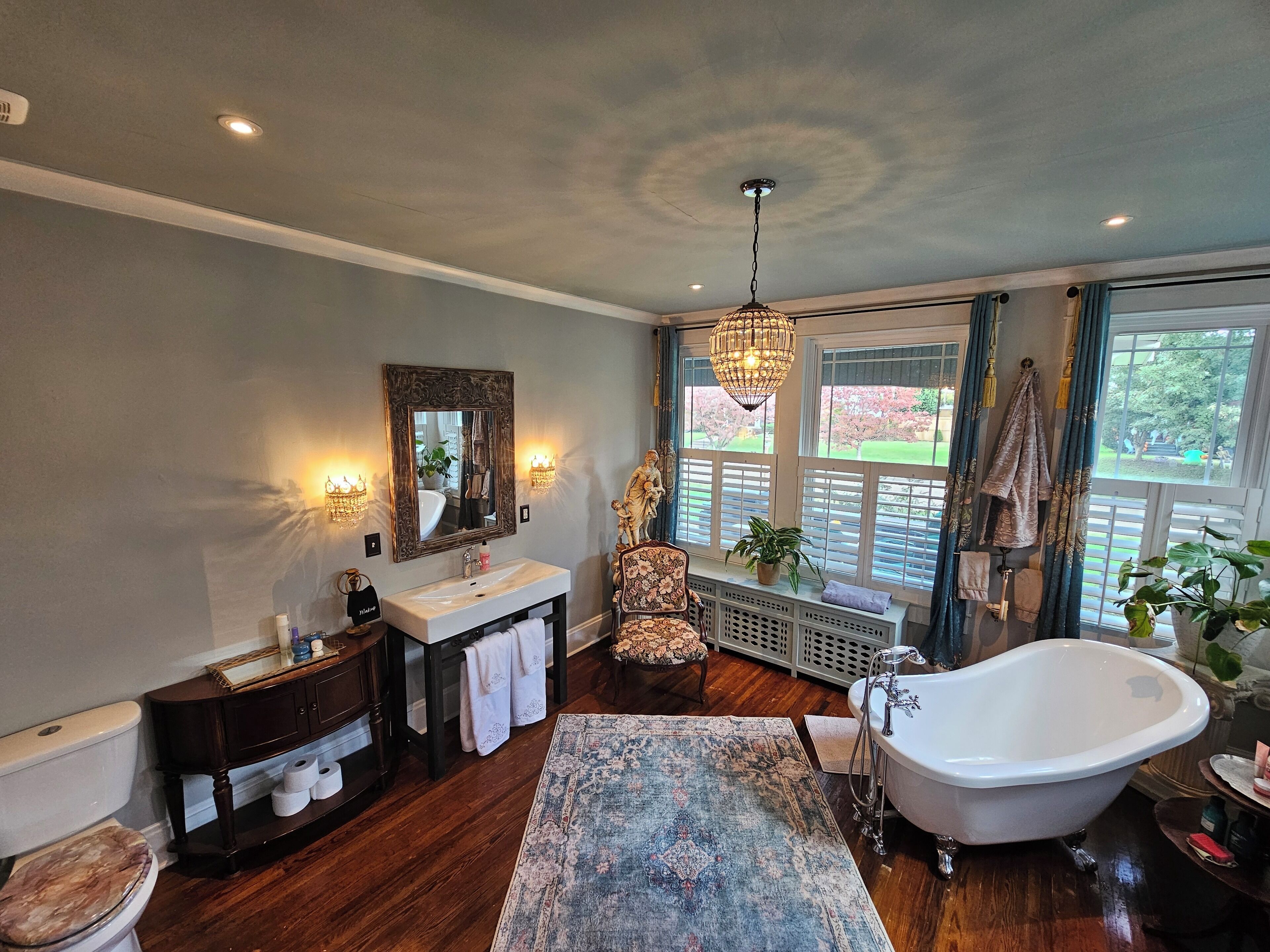 Une salle de bain avec une baignoire sur pieds, un meuble-lavabo avec un miroir, des toilettes et une fenêtre avec des volets.