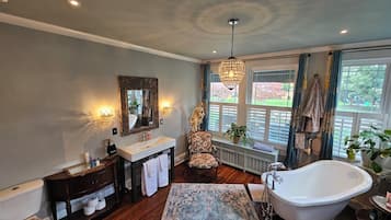 Une salle de bain avec une baignoire sur pieds, un meuble-lavabo avec un miroir, des toilettes et une fenêtre avec des volets.