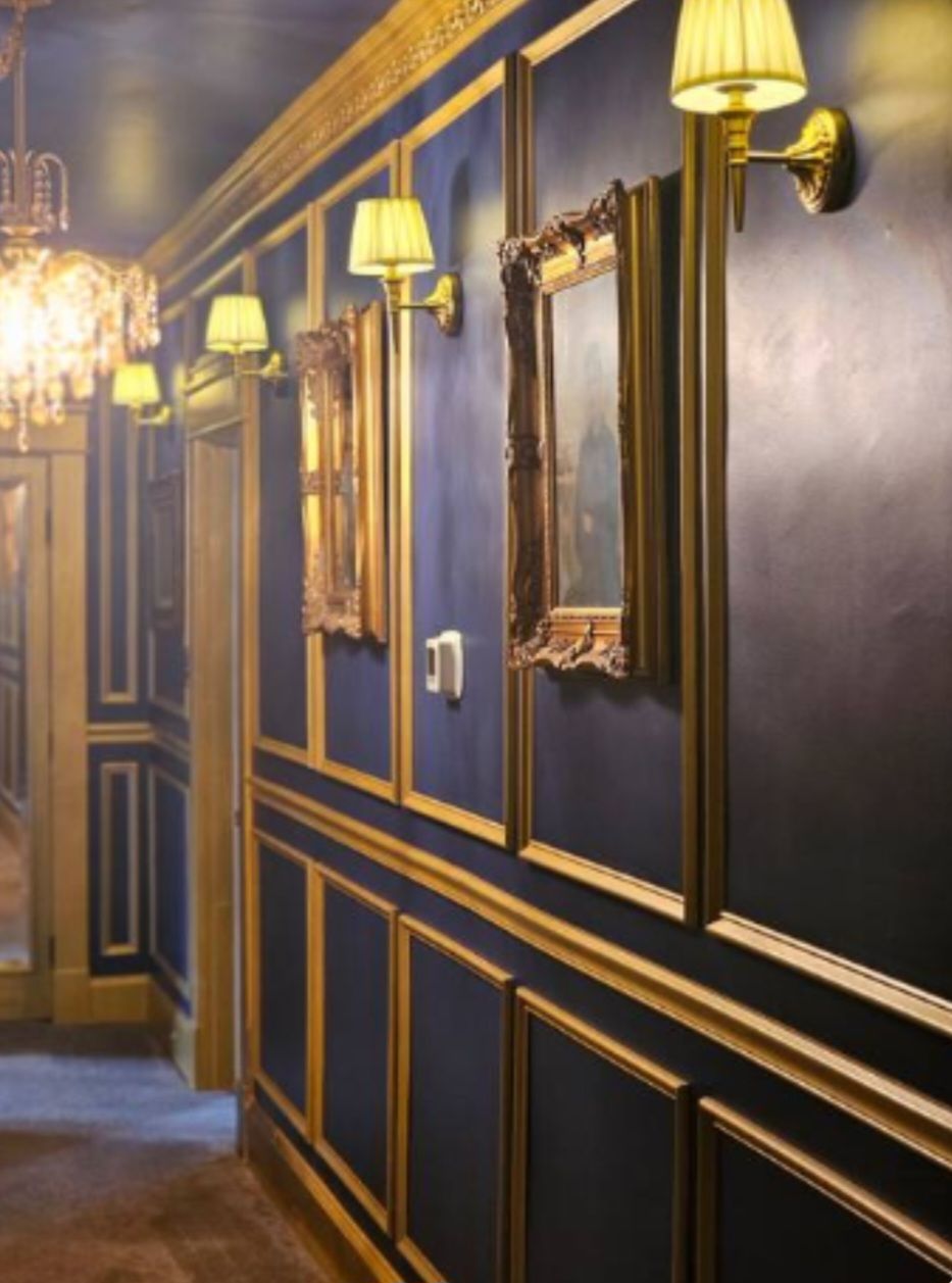 A hallway with ornate wall sconces, a mirror, and a chandelier.