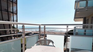 En balkong med ett bord och stolar, med utsikt över en strand och en klar himmel.