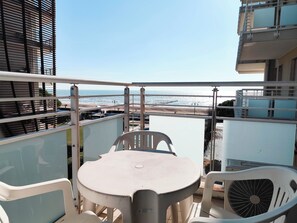 Ein Balkon mit Tisch und Stühlen mit Blick auf einen Strand und einen klaren Himmel.